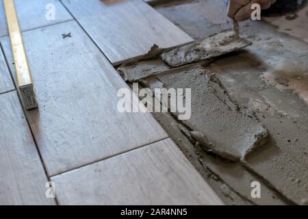 Man installing rectangular shaped floor tiles in kitchen. Applying adhesive before installation and verifying afterwards Stock Photo