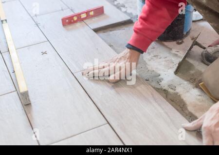 Man installing rectangular shaped floor tiles in kitchen. Applying adhesive before installation and verifying afterwards Stock Photo