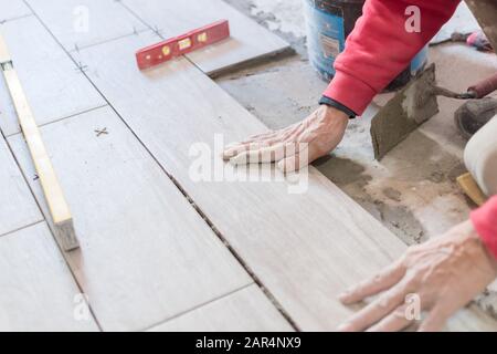 Man installing rectangular shaped floor tiles in kitchen. Applying adhesive before installation and verifying afterwards Stock Photo