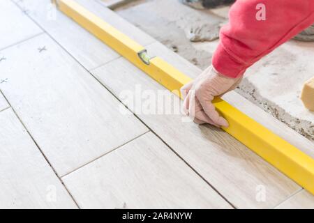 Man installing rectangular shaped floor tiles in kitchen. Applying adhesive before installation and verifying afterwards Stock Photo