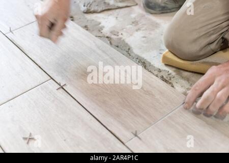 Man installing rectangular shaped floor tiles in kitchen. Applying ...