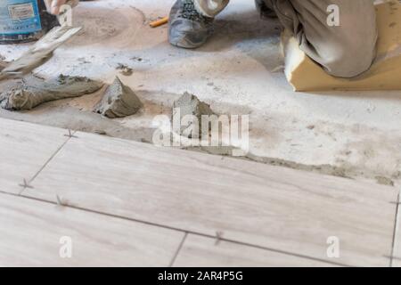 Man installing rectangular shaped floor tiles in kitchen. Applying adhesive before installation and verifying afterwards Stock Photo