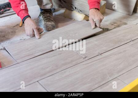 Man installing rectangular shaped floor tiles in kitchen. Applying adhesive before installation and verifying afterwards Stock Photo