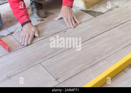 Man installing rectangular shaped floor tiles in kitchen. Applying adhesive before installation and verifying afterwards Stock Photo