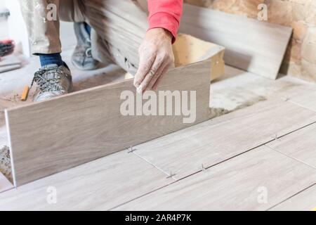 Man installing rectangular shaped floor tiles in kitchen. Applying adhesive before installation and verifying afterwards Stock Photo