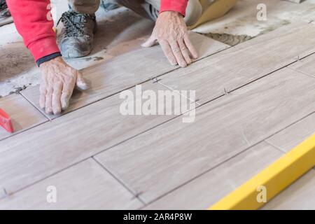 Man installing rectangular shaped floor tiles in kitchen. Applying ...