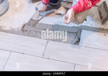 Man installing rectangular shaped floor tiles in kitchen. Applying adhesive before installation and verifying afterwards Stock Photo