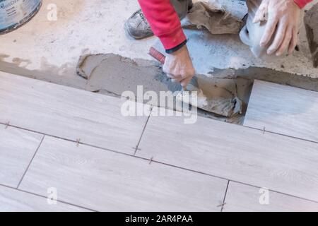 Man installing rectangular shaped floor tiles in kitchen. Applying adhesive before installation and verifying afterwards Stock Photo