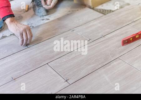 Man installing rectangular shaped floor tiles in kitchen. Applying adhesive before installation and verifying afterwards Stock Photo