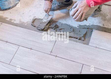 Man installing rectangular shaped floor tiles in kitchen. Applying adhesive before installation and verifying afterwards Stock Photo
