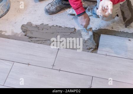 Man installing rectangular shaped floor tiles in kitchen. Applying adhesive before installation and verifying afterwards Stock Photo