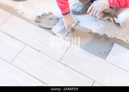 Man installing rectangular shaped floor tiles in kitchen. Applying ...