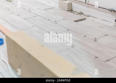 Man installing rectangular shaped floor tiles in kitchen. Applying adhesive before installation and verifying afterwards Stock Photo