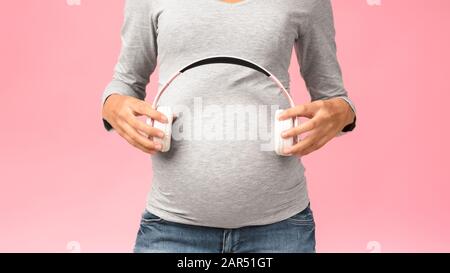 Pregnant woman holding headphones on belly Stock Photo
