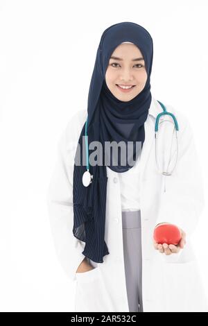 Asian young adult attractive muslim woman doctor wearing hijab standing with stethoscope and holding red heart isolated in white background. Healthcar Stock Photo