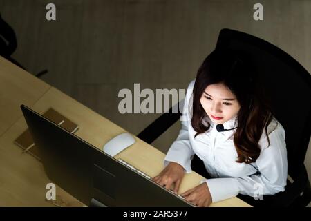 Late Night Environment. Top view of young adult friendly operator call center with headsets working hard at night. Using for 24 Hr. 7 days Call centre Stock Photo