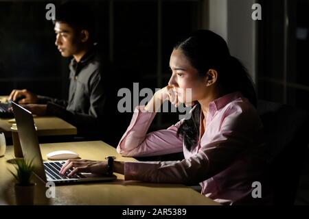 Young adult asian businessman and woman working late at night in their office with desktop computer and laptop. Using as hard working and working late Stock Photo