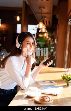 Successful female young adult asian freelancer working in cafe using her mobile phone and coffee breakfast set. Stock Photo