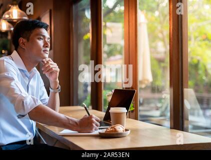 Focused asian college student working with laptop in cafe preparing for test or exam. Stock Photo