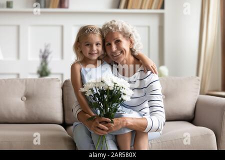 Portrait of happy mature woman holding on lap little princess. Stock Photo