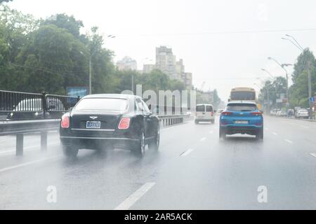 Kyiv, Ukraine - May 25th, 2019:Wet highway after heavy rain with warm sunset evening sun on background. Bentley vehicle riding high speed by rainy Stock Photo