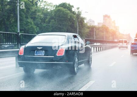 Kyiv, Ukraine - May 25th, 2019:Wet highway after heavy rain with warm sunset evening sun on background. Bentley vehicle riding high speed by rainy Stock Photo