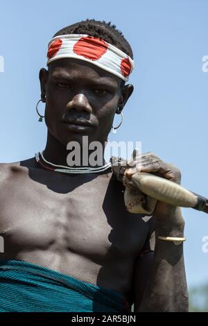 Portrait of young Mursi warrior holding a gun. The Mursi (or Murzu) are a Sub-Saharan African nomadic cattle herder tribe located in the Omo valley in Stock Photo
