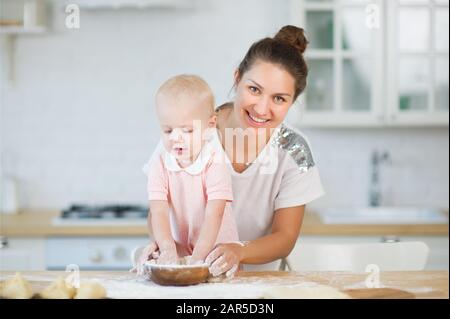 a young woman hugs a little daughter from the back, holding in her hand a wooden plate Stock Photo