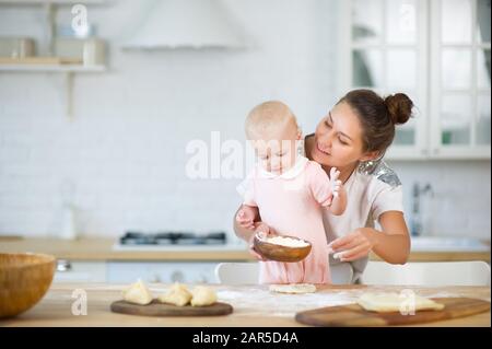 a young woman hugs a little daughter from the back, holding in her hand a wooden plate Stock Photo