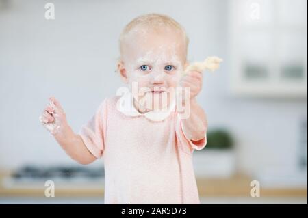 blue-eyed girl with a face in flour holds a piece of dough in his hand Stock Photo