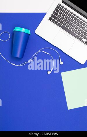 office workplace. laptop keyboard, notebook with mockup, mug and headphones lie on a blue surface Stock Photo