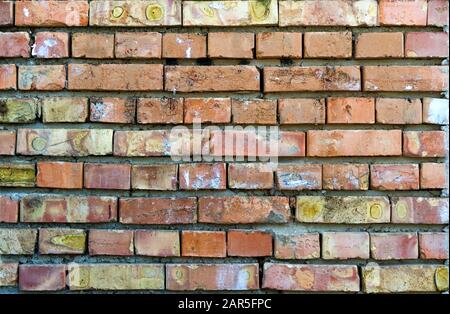 A wall of bricks, roughly laid out with heterogeneous spots and cracked paint Stock Photo