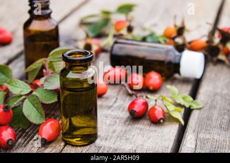 Glass bottle of rosehip essential oil with fresh rosehips on a wooden table. Tincture or essential oil with rose hips. Spa herbal medicine. Stock Photo