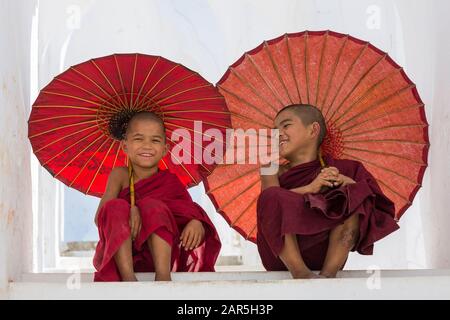 Young novice Buddhist monks holding parasols at Myatheindan Pagoda (also known as Hsinbyume Pagoda), Mingun, Myanmar (Burma), Asia in February Stock Photo