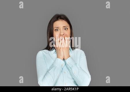 Freestyle. Young woman standing isolated on grey covering mouth scared Stock Photo