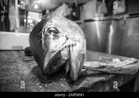 Grey-scale shot of a dead fish on a wooden table in the kitchen Stock Photo
