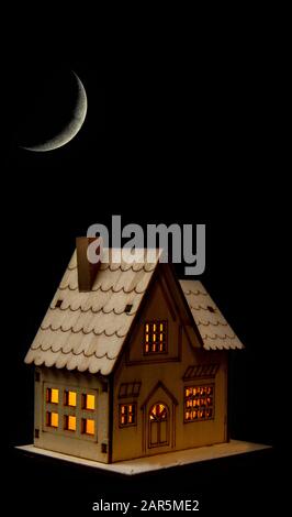Toy house with lights on at night under a crescent moon. Leaving the lights on, waste of electricity, power, not eco friendly. Stock Photo