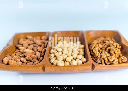 Close-up of healthy raw snack of nuts served in a wooden container, isolated on white background. Raw almonds, raw hazelnuts, raw walnuts. Stock Photo