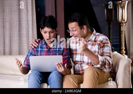 Father and son astonished on receiving good news using laptop Stock Photo