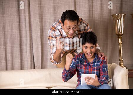 Father and son astonished on receiving good news using digital tablet Stock Photo