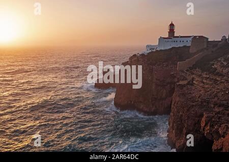 Yellow sunset disk going into the ocean with a lighthouse on a cliff Stock Photo