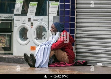 A homeless man sits on the wet pavement outside the Emmaus Preston homeless charity store.  Emmaus Preston is an independent local charity store. Stock Photo