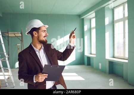 Foreman bearded man in a white helmet in a room at a construction site Stock Photo