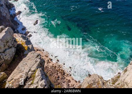 View over the cliffs at the deep ocean and waves swirling at small beach and rocks at Cape Point near Cape Town South Africa Stock Photo