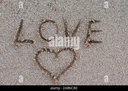 The word love is written with a finger in the sand on a beach. love message written in sand. Stock Photo