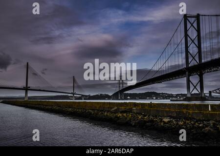 Forth Road Bridge and Queensferry Crossing bridges over the Forth Estuary in Scotland with dramatic skies, pier in foreground Stock Photo