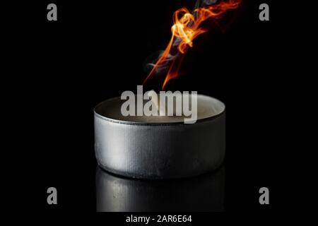 One burning tea candle isolated on black glass Stock Photo