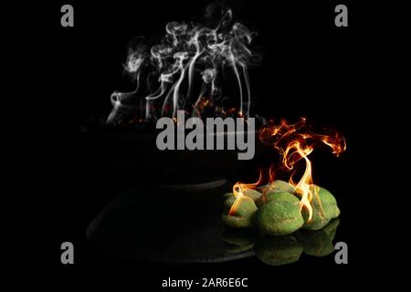 Burning green wasabi peanuts with burnt smoking in bowl isolated on black glass Stock Photo