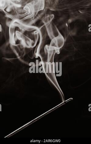 sepia toned black and white vertical photo of a smoking incense stick Stock Photo