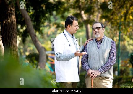 Doctor talking with senior man in hospital garden Stock Photo